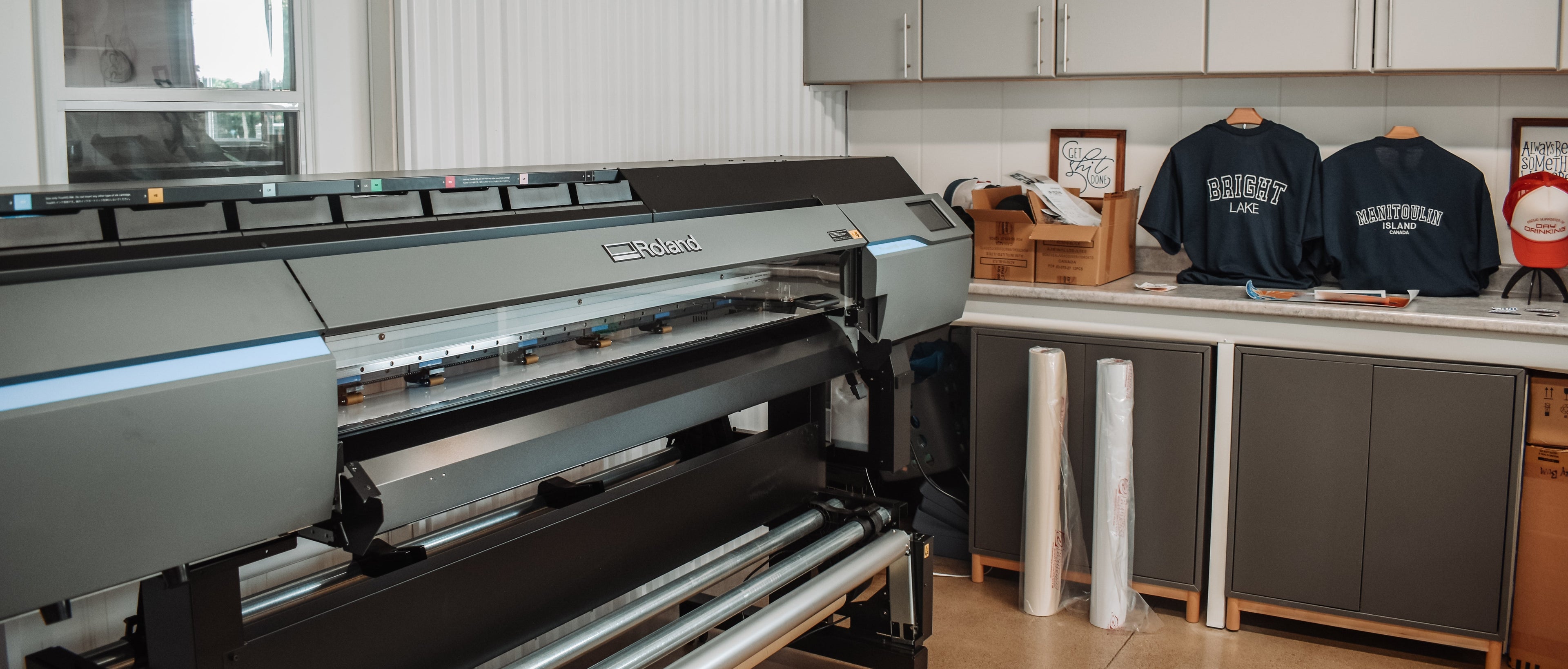 Large printing machine in a room with cabinets and clothing items.
