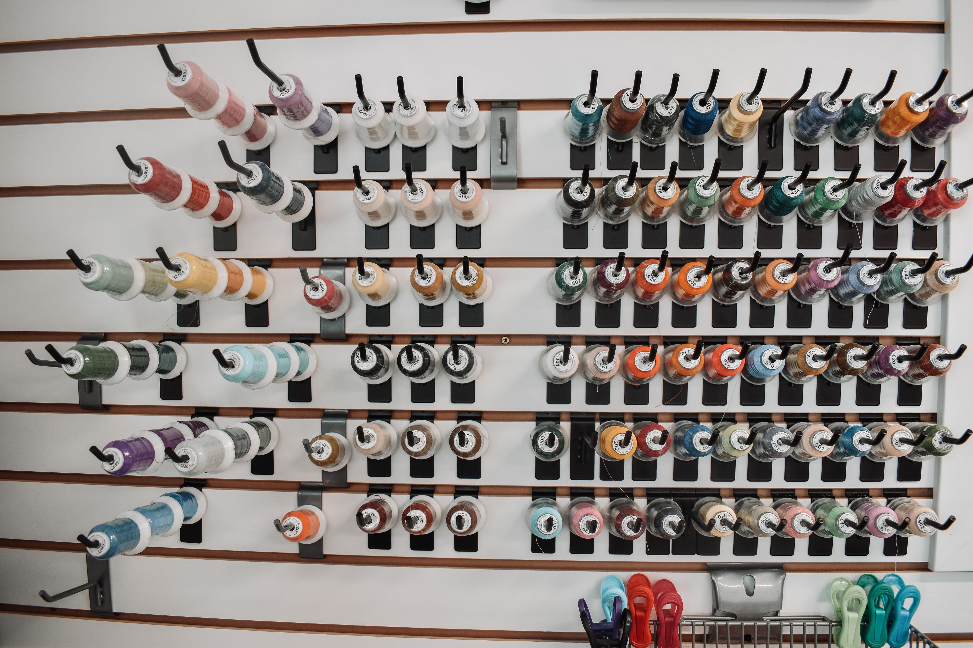 Spools of thread in various colors arranged on a wall-mounted rack.